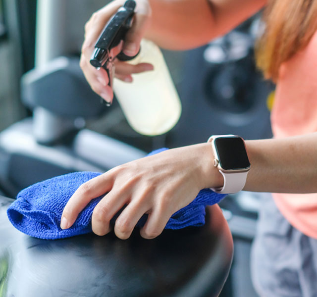 Woman using cleaning supplies to clean fitness equipment