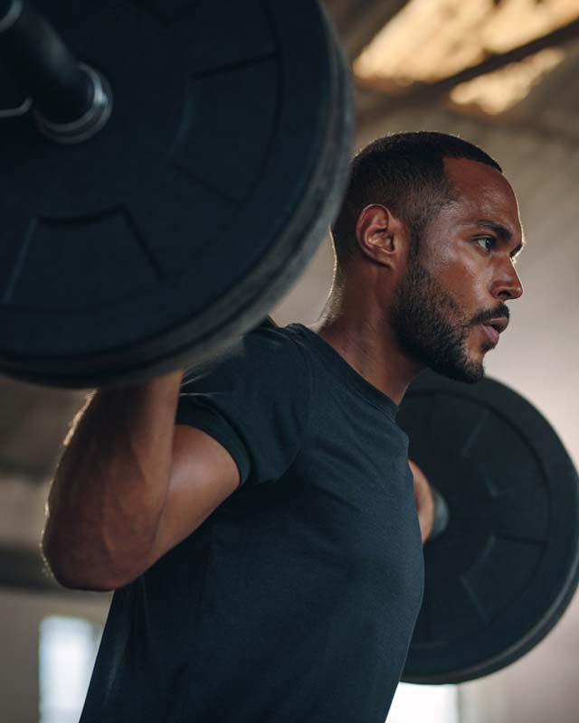 Man with a heavy barbell over his shoulders looking determined while working out