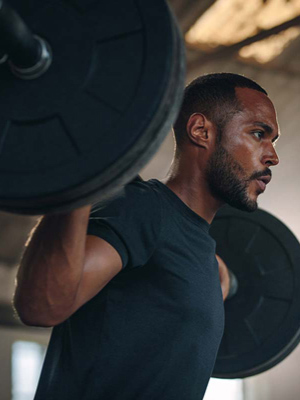 Man with a heavy barbell over his shoulders looking determined while working out