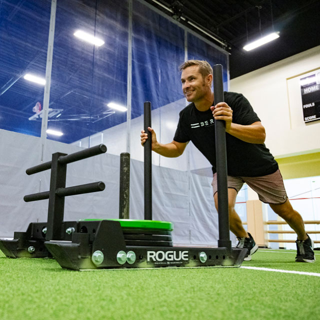 Man pushing a weighted sled inside The Edge Performance Training center