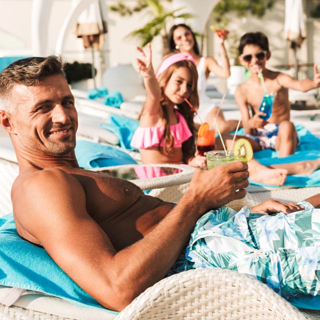 Happy family of four lounging by the pool with poolside drinks