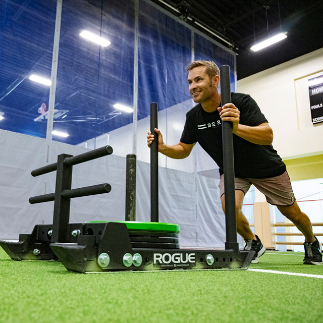 Man training on The Edge open training turf pushing a weighted sled