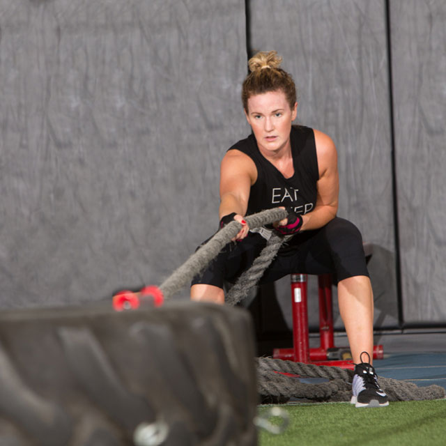 Woman training on the Edge open turf training space pulling a tire