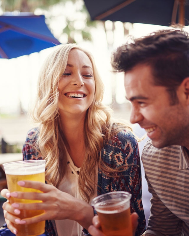 A man and woman laughing and smiling while enjoying beers on the patio of Citrus Fresh Grill
