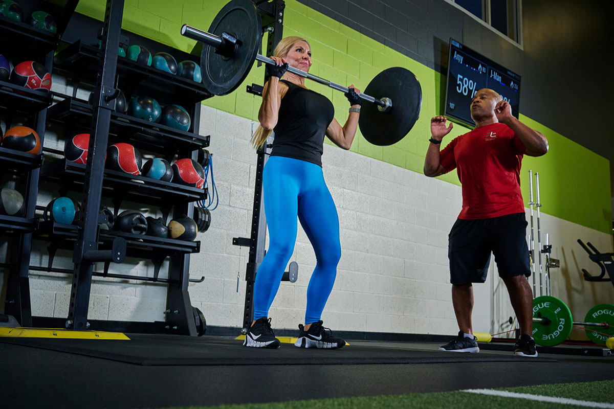 A women lifting heavy weights with her personal trainer in The Edge Performance Training space