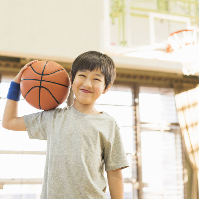 A little boy holding a basketball looking happy during Breakthrough Sports Basketball program