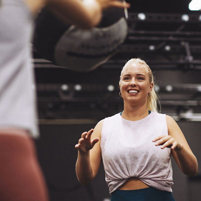 Woman smiling while performing a partner exercise in a Rev32 weight loss fitness and nutrition program