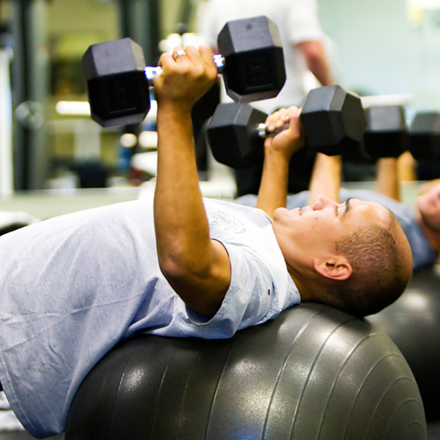 Man on an exercise ball doing chest presses with dumbbells in a Rev32 fitness class