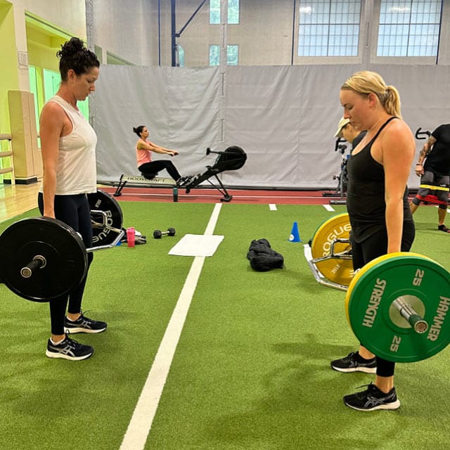 Two women holding barbells with weights in a Rev32 workout class