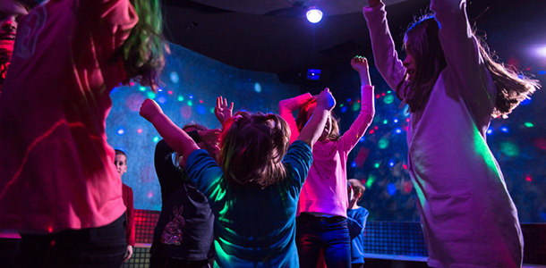 A bunch of kids dancing in the dark with neon lights