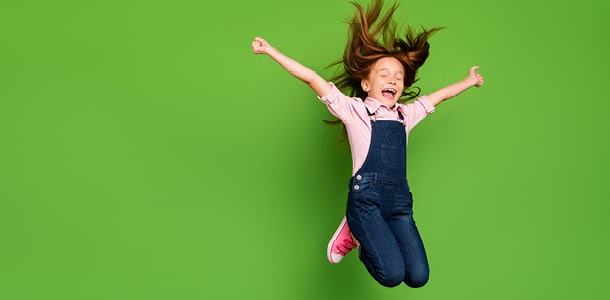 A 5-year-old girl jumping with a big smile on her face in front of a green background