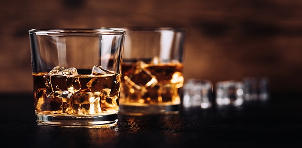 Two glasses of scotch on the rocks sitting on a bar