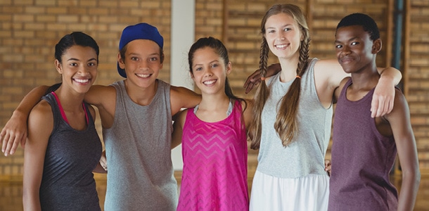 Group of teenagers with their arms around each other's shoulders smiling in fitness clothes