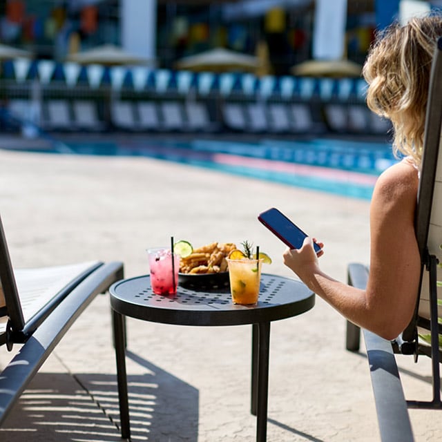 A woman enjoying poolside drinks and food from the Splash Pool Bar
