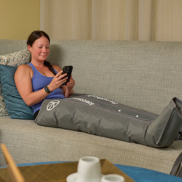 A woman relaxing in Therabody compression sleeves recovery boots